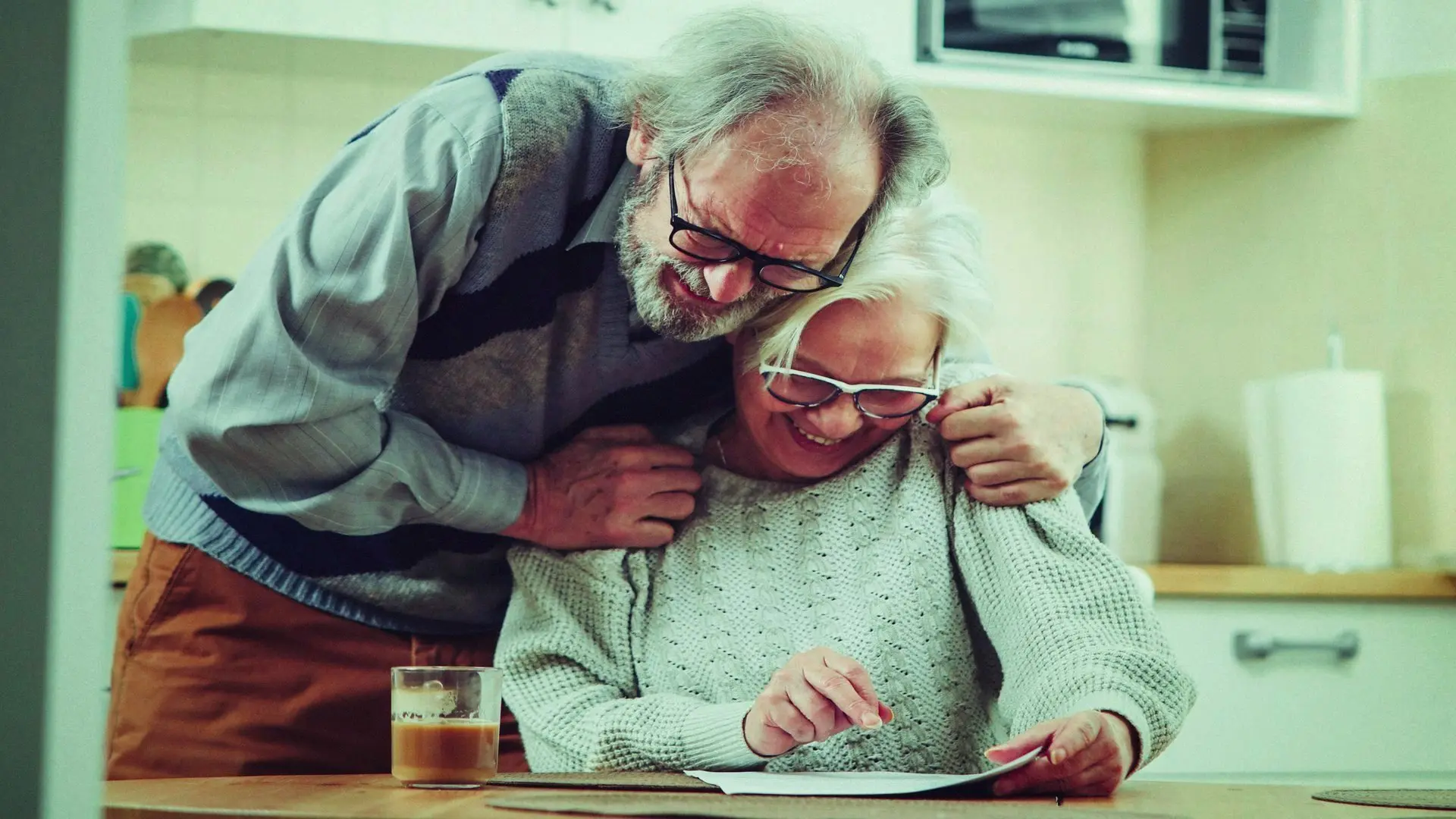An elderly couple hugging with joy of receiving a letter